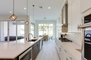 Una cucina moderna con una grande isola, elettrodomestici in acciaio inossidabile e illuminazione a sospensione.