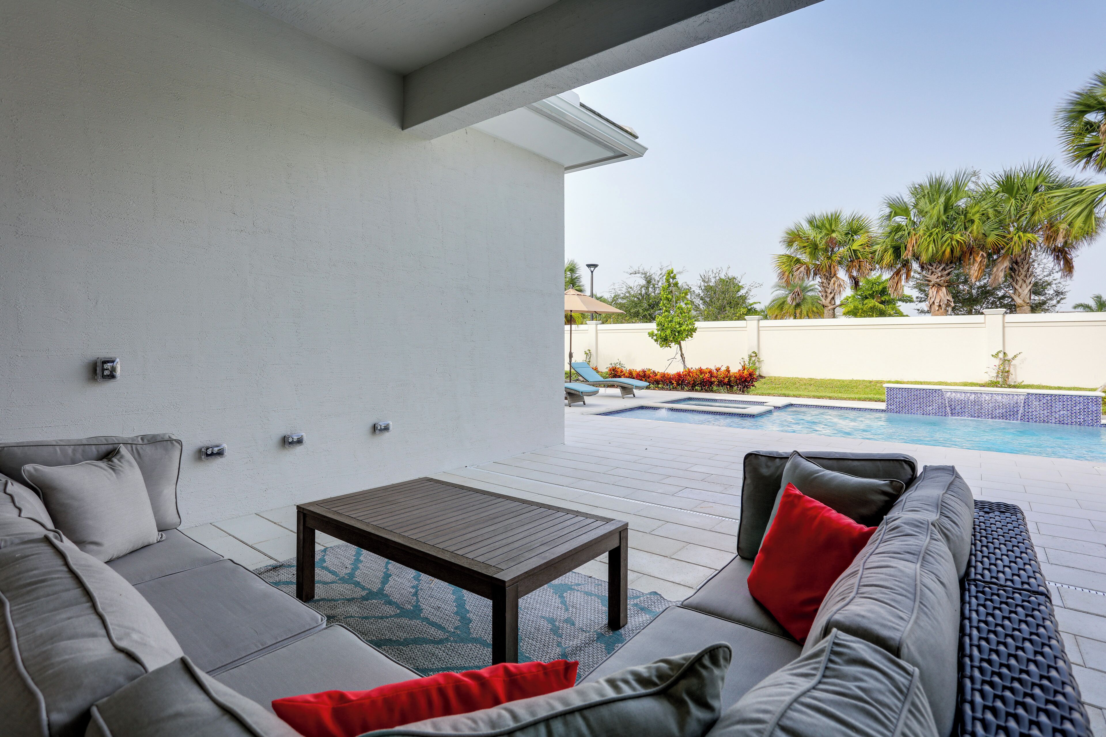 A modern outdoor patio with a gray sofa, a wooden table, and a pool in the background.