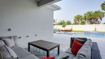 A modern outdoor patio with a gray sofa, a wooden table, and a pool in the background.