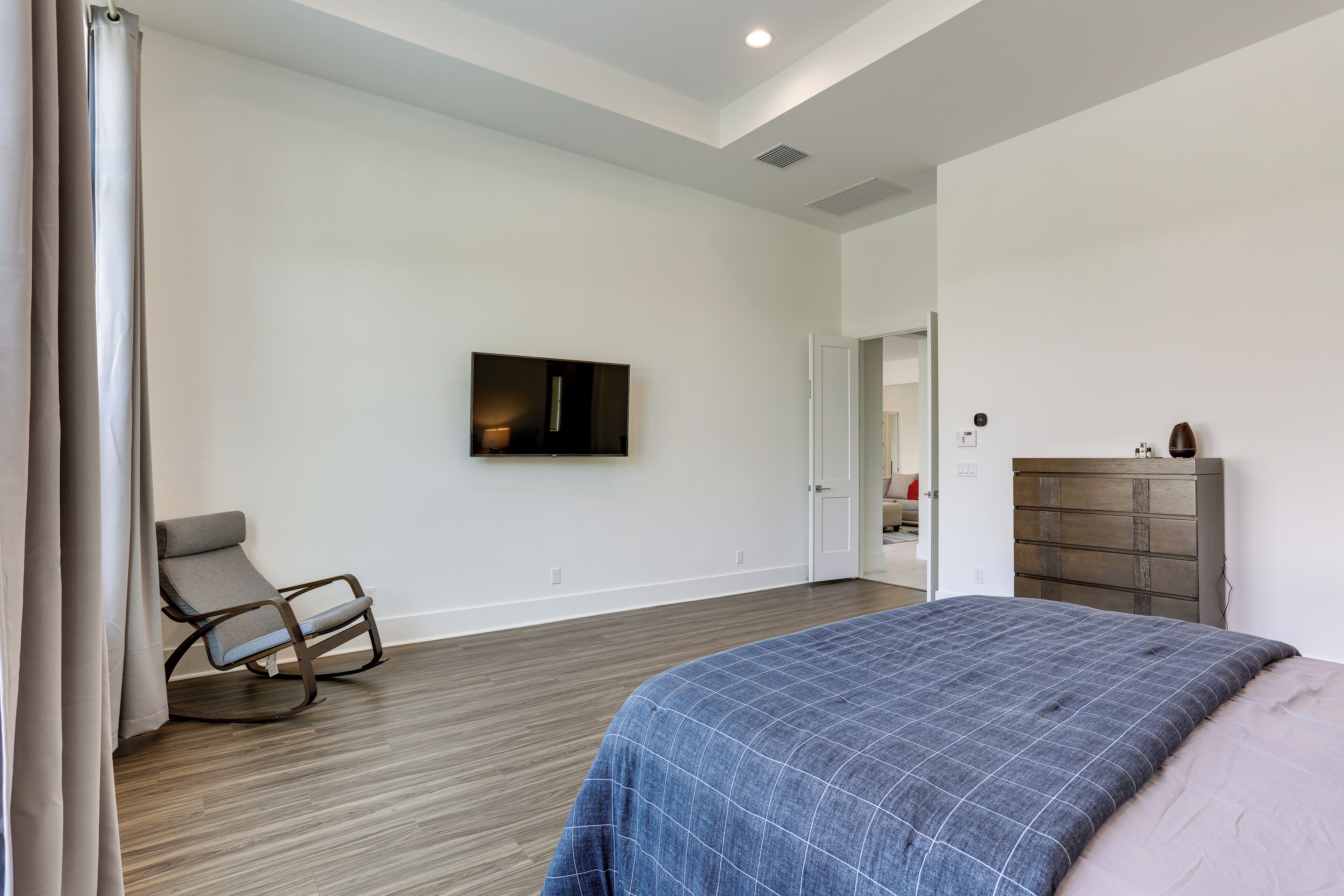 A bedroom with a bed, a rocking chair, a dresser, and a TV on the wall.