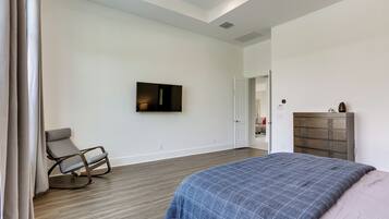 A bedroom with a bed, a rocking chair, a dresser, and a TV on the wall.