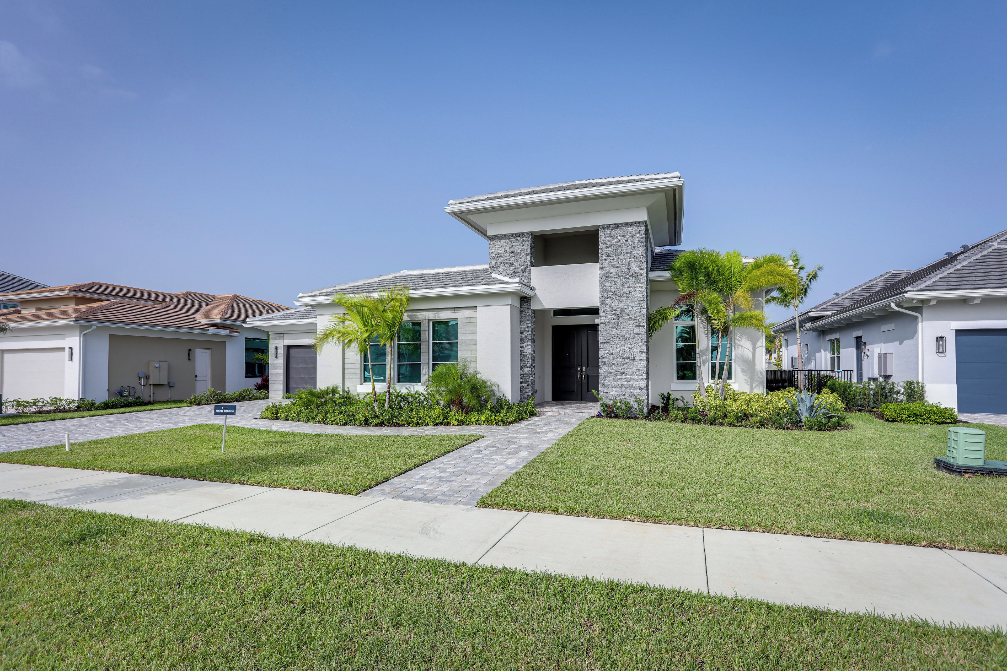 A modern two-story house with a stone facade, large windows, and a well-maintained lawn.