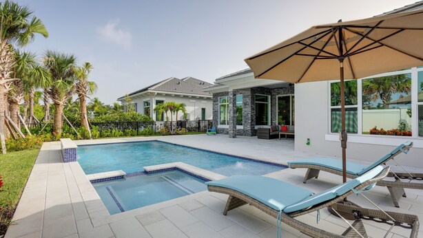 A swimming pool with lounge chairs and an umbrella, surrounded by palm trees and a house. - Private Pool & Spa: Luxe Palm Beach Gardens Home (West Palm Beach)