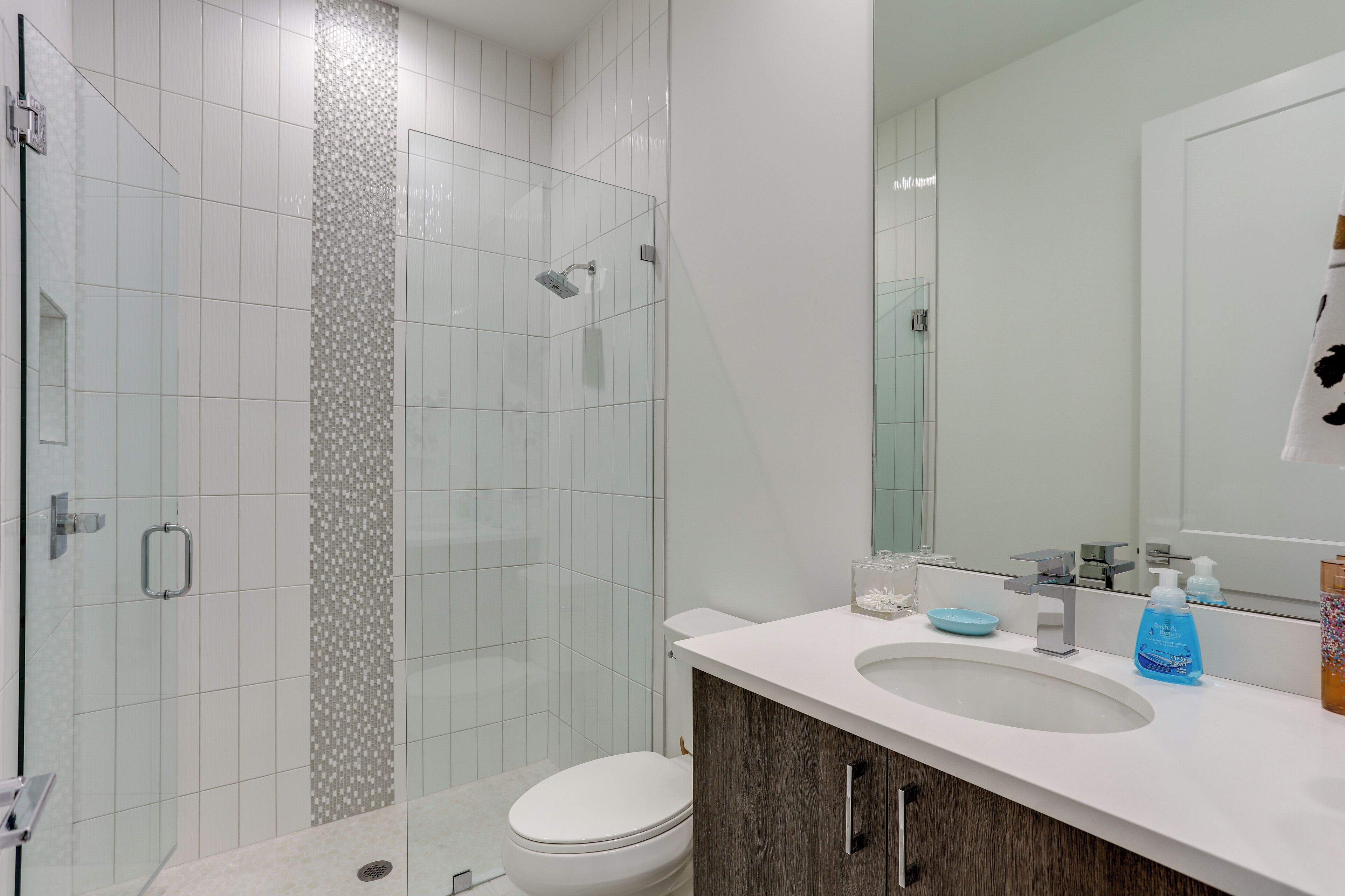 A modern bathroom with a glass-enclosed shower, a white toilet, and a sink with a mirror above it.