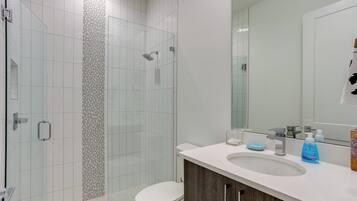A modern bathroom with a glass-enclosed shower, a white toilet, and a sink with a mirror above it.