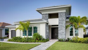 A modern two-story house with a stone facade, large windows, and a well-maintained lawn. - Private Pool & Spa: Luxe Palm Beach Gardens Home (West Palm Beach)
