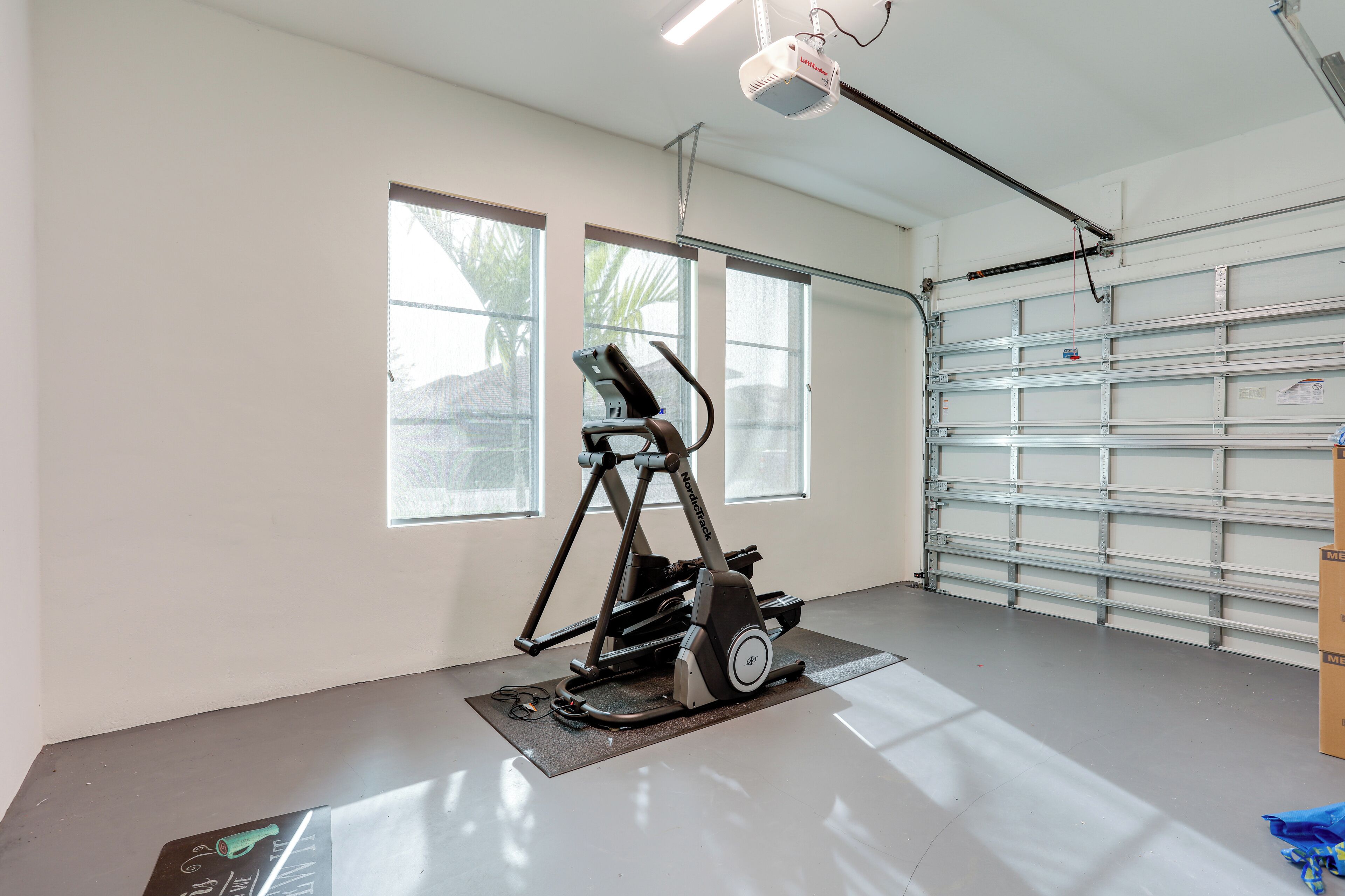 A spacious garage with a stationary exercise bike, large windows, and a garage door.