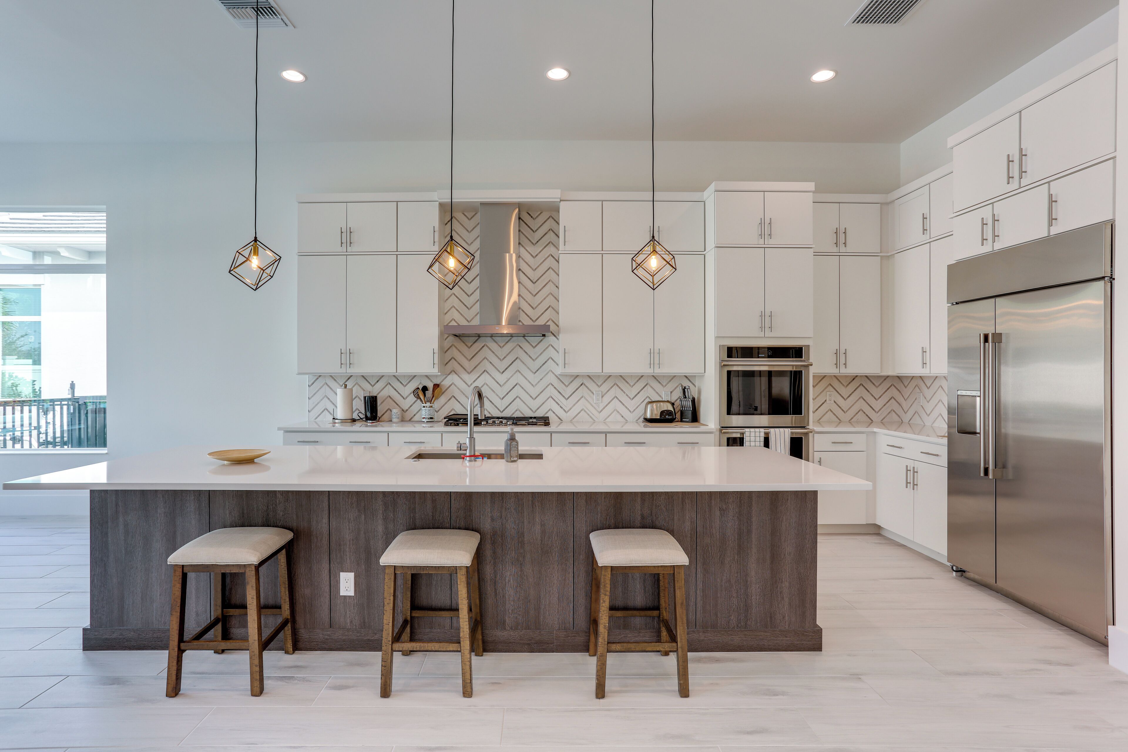 A modern kitchen with a large island, pendant lights, and stainless steel appliances.