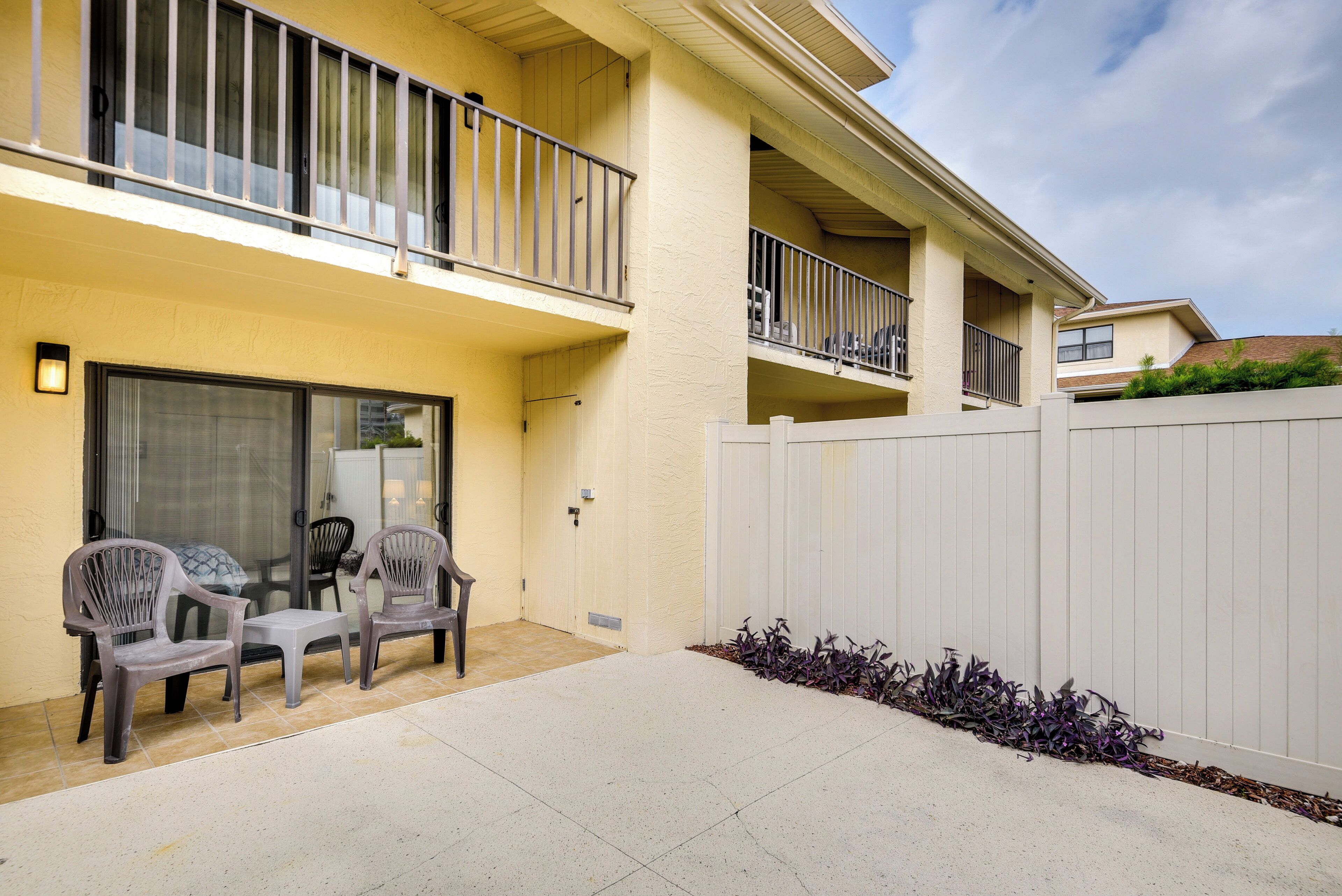 A two-story building with a balcony, a patio with chairs, and a white fence.