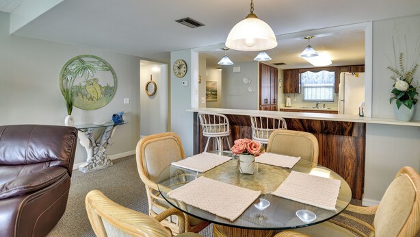 A dining area with a glass table, cushioned chairs, and a hanging light fixture. - Daytona Beach Shores Condo Rental: Walk to Beach! (Daytona Beach)