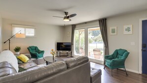 A living room with a grey sofa, two green armchairs, a flat-screen TV, a ceiling fan, and a window with blinds. - Lovely South Bend Home ~ 3 Mi to Dtwn & Notre Dame (South Bend)