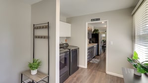 A laundry area with a drying rack, washing machine, and dryer. There is a hallway leading to a kitchen area with cabinets and a microwave. - Lovely South Bend Home ~ 3 Mi to Dtwn & Notre Dame (South Bend)