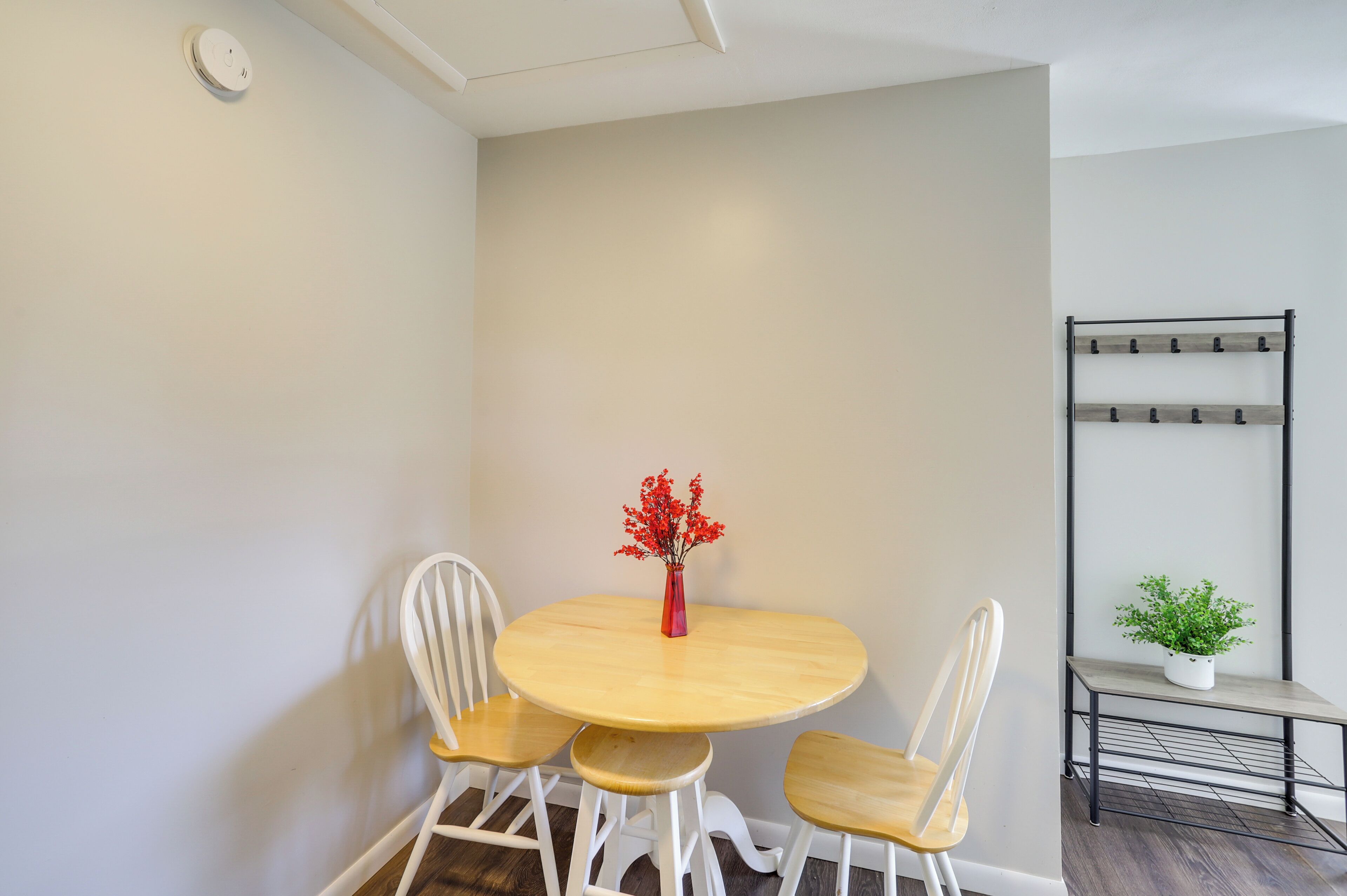 A small dining area with a round wooden table, two white chairs, and a vase with red flowers.