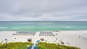En strand med rader av blå parasoller och solstolar, en sandstrand och havet i bakgrunden.