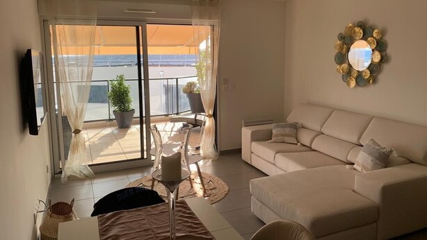 Ein Wohnzimmer mit einem beigen Sofa, einem Glastisch und Meerblick durch eine Schiebetür.