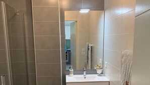 Ein modernes Badezimmer mit einer begehbaren Dusche, einem weißen Waschtisch mit Spiegel und einem Handtuchhalter.