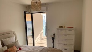 Ein Schlafzimmer mit Bett, Kommode und Blick nach draußen.