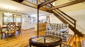 Ein geräumiger Wohnbereich mit Holzboden, einem runden Glastisch, einem karierten Sofa und einer Treppe, die in ein Obergeschoss führt.