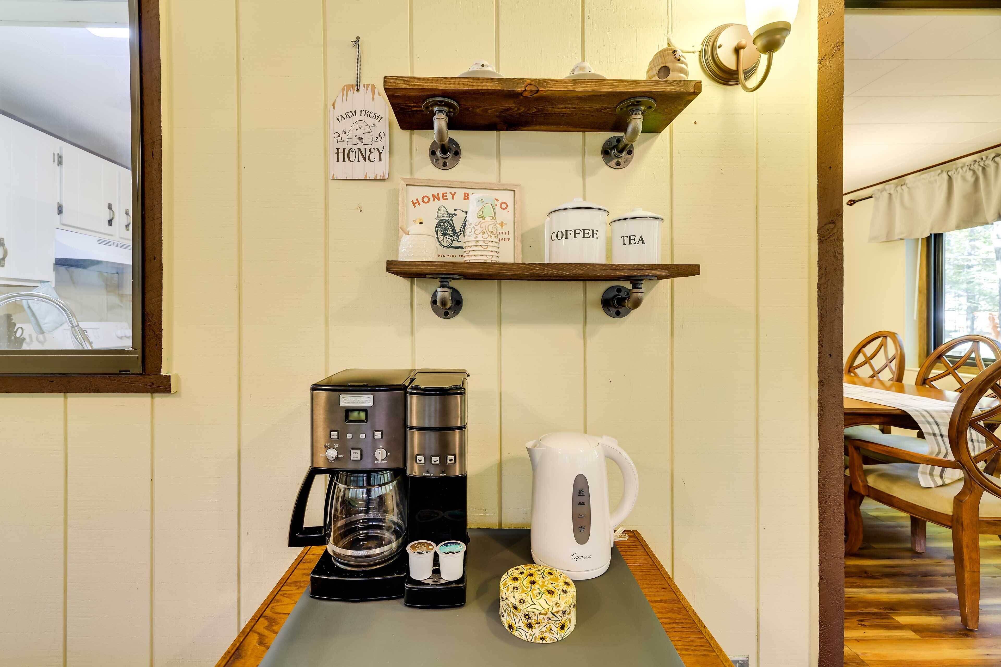 Eine Küchenzeile mit Kaffeemaschine, Wasserkocher und einer Ablage mit Gläsern, beschriftet mit 'Kaffee' und 'Tee'.