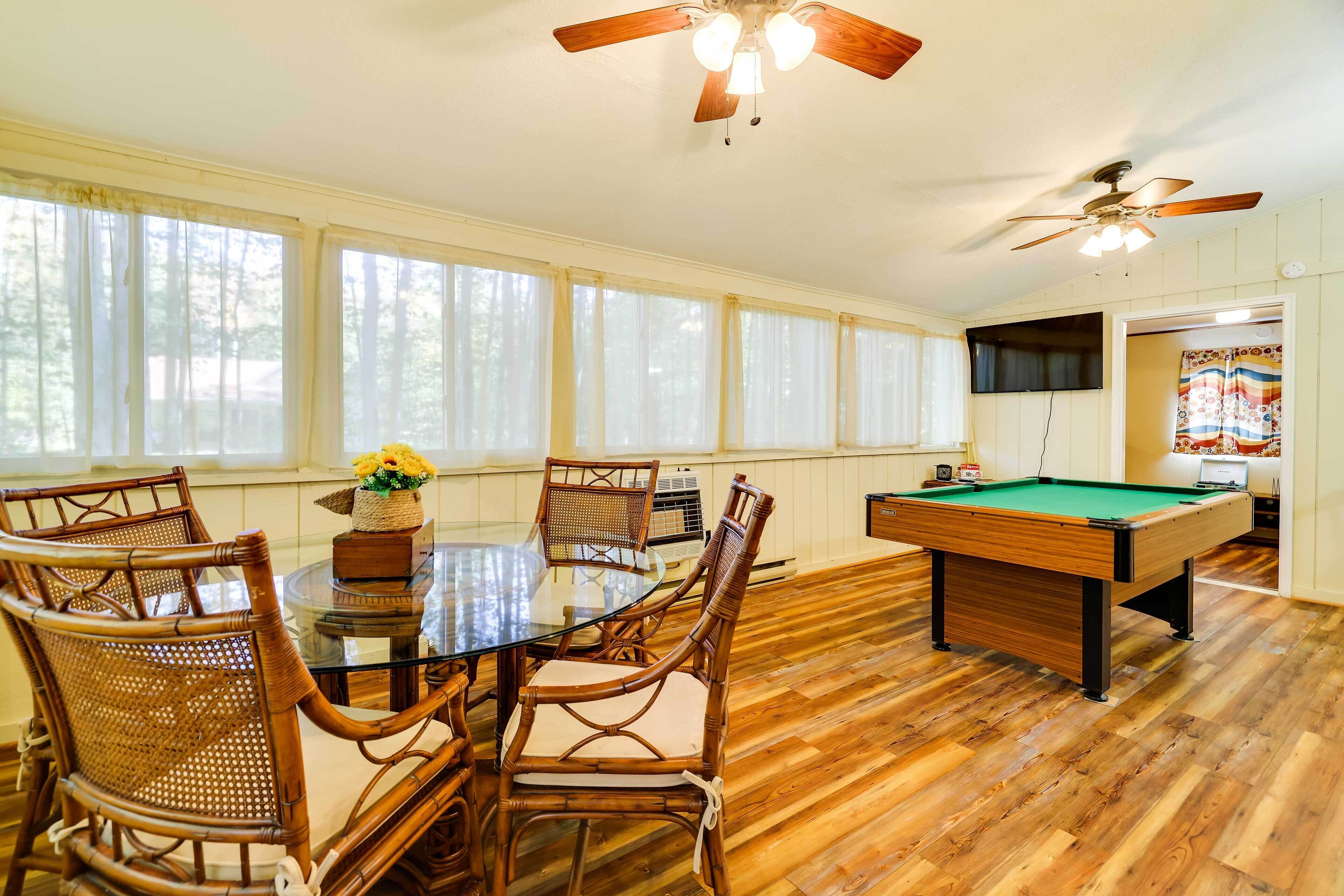 A room with a pool table, wooden flooring, and a ceiling fan.