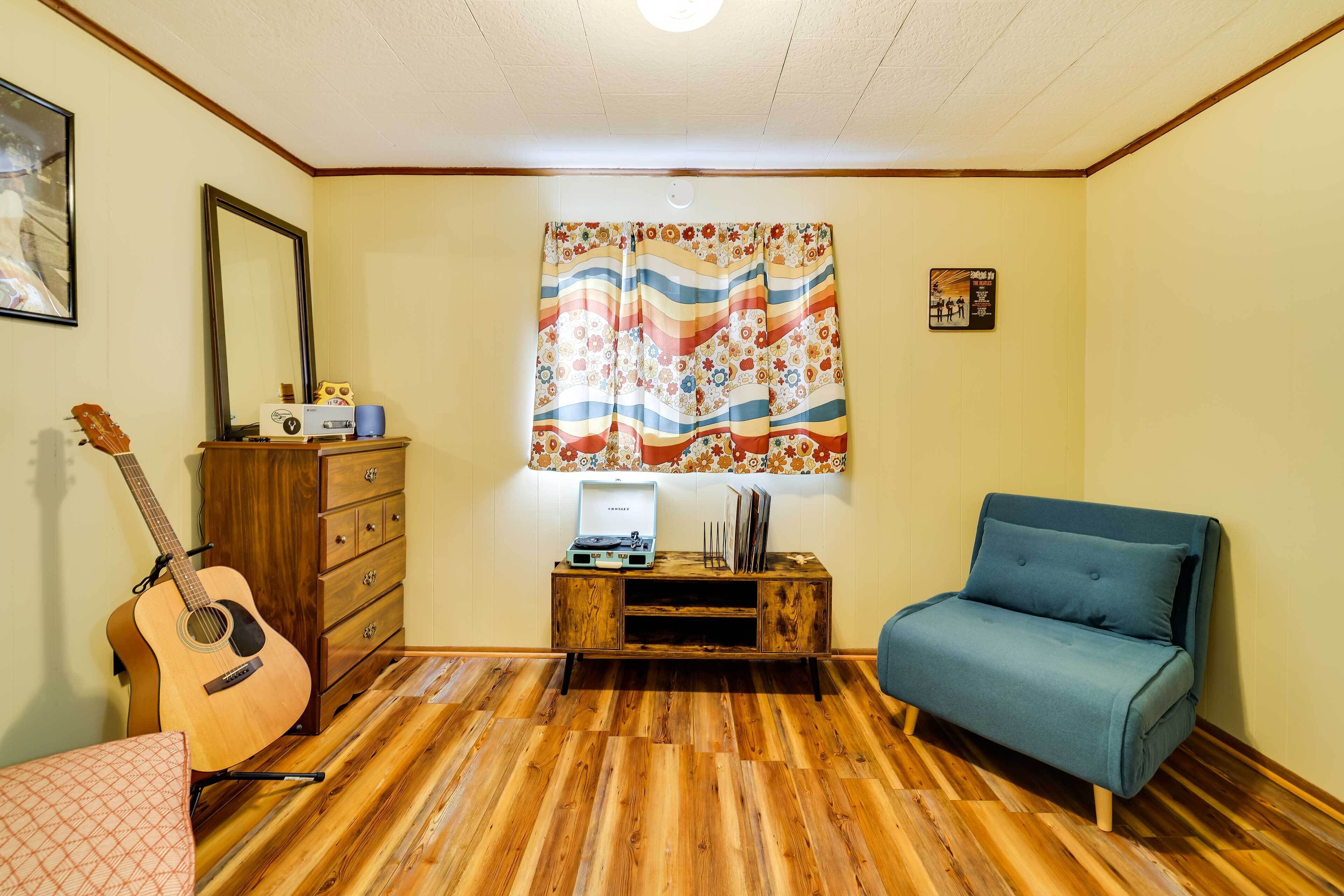 Ein Zimmer mit Holzboden, einem blauen Sofa, einer Gitarre, einem Holzschrank und einem wandmontierten Spiegel.