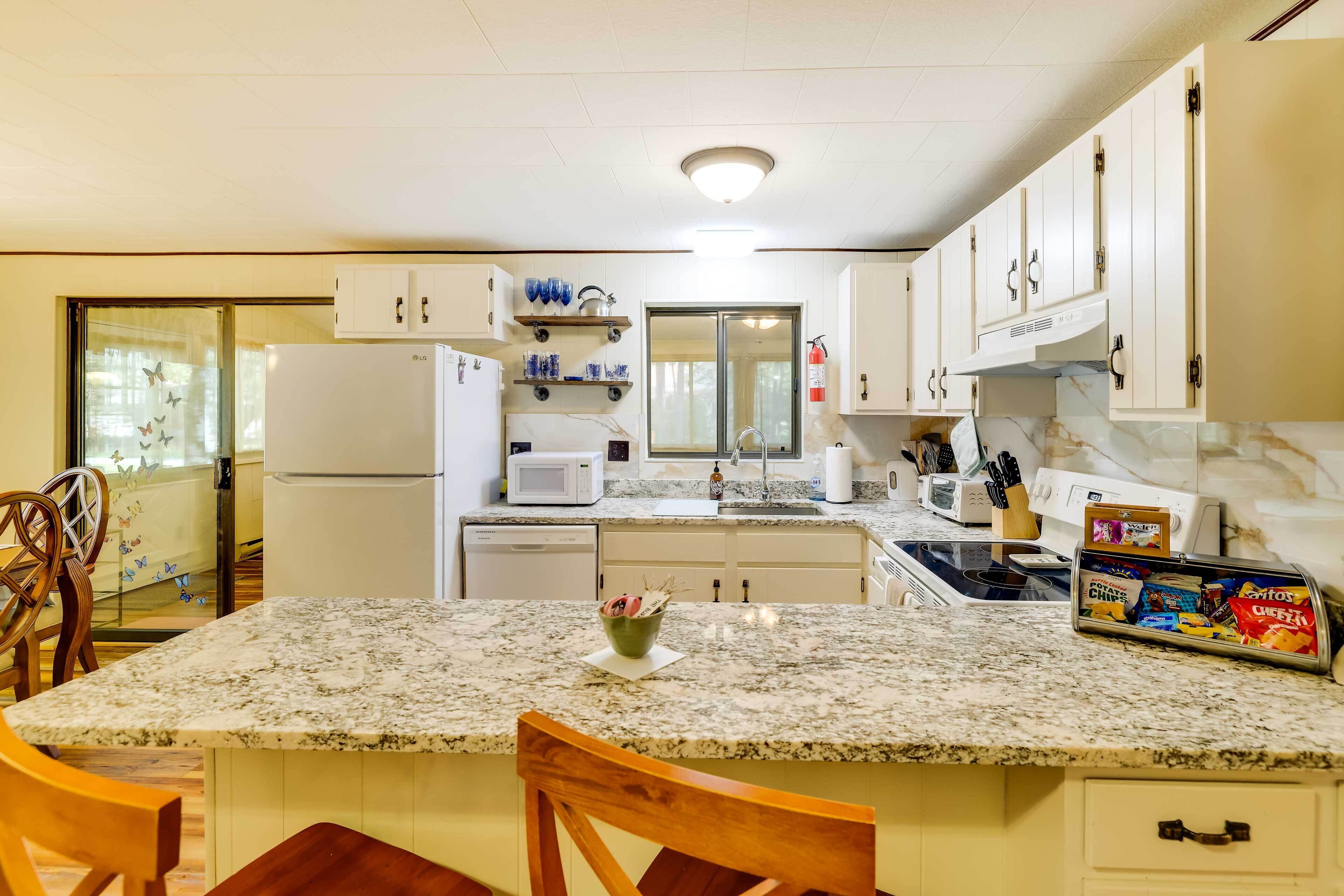 A kitchen with white cabinets, a granite countertop, a refrigerator, a microwave, a sink, and a dining area with two wooden chairs.