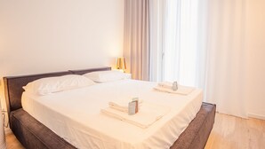 A neatly made bed with white linens, a bedside lamp, and a folded towel with toiletries on the side. - Garda Luxury Suite - One Bedroom Apartment, Sleeps 2 (Padenghe sul Garda)