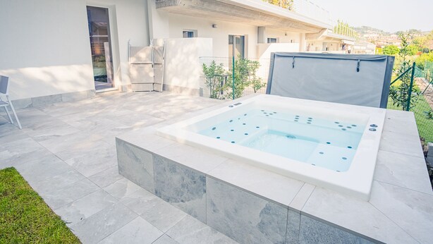 A modern outdoor hot tub area with a stone border, a covered seating area, and a view of a residential neighborhood. - Garda Luxury Suite - One Bedroom Apartment, Sleeps 2 (Padenghe sul Garda)