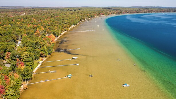 An aerial view of a coastal area with a clear beach, boats, and dense forest. - Higgins Lake Cottage w/ Private Fire Pit & Grill! (Roscommon)
