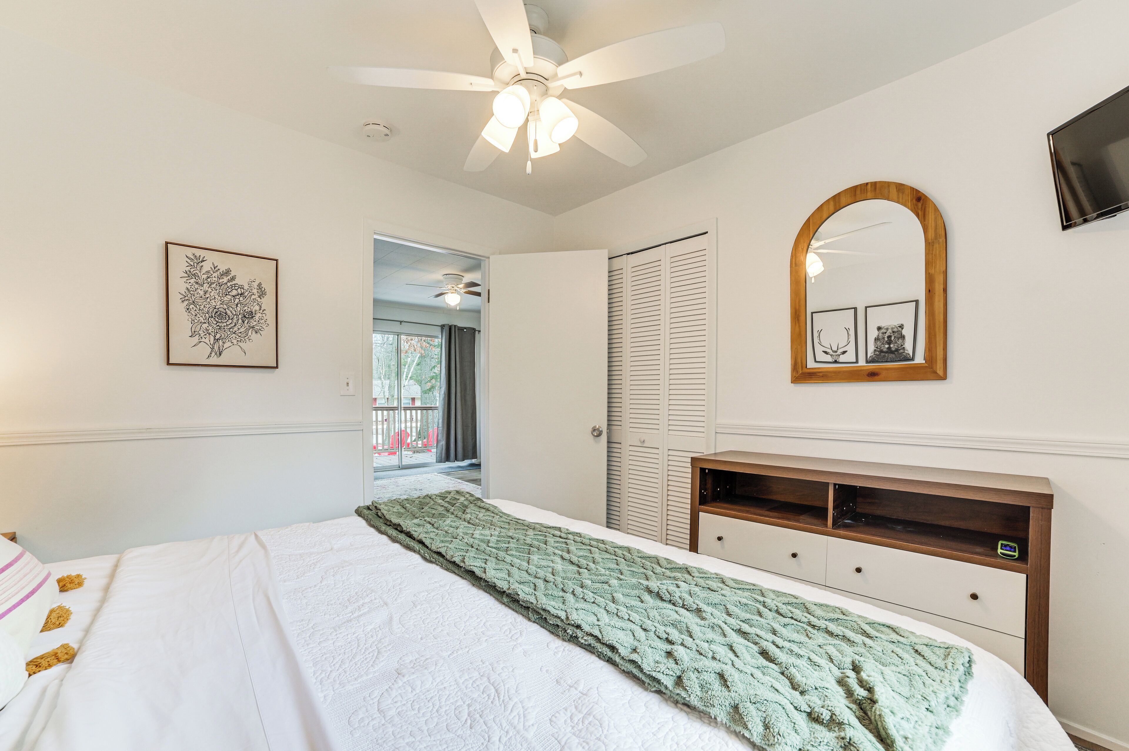 Une chambre à coucher avec un lit, un ventilateur de plafond, une tête de lit en bois, un miroir et un tableau encadré accroché au mur.
