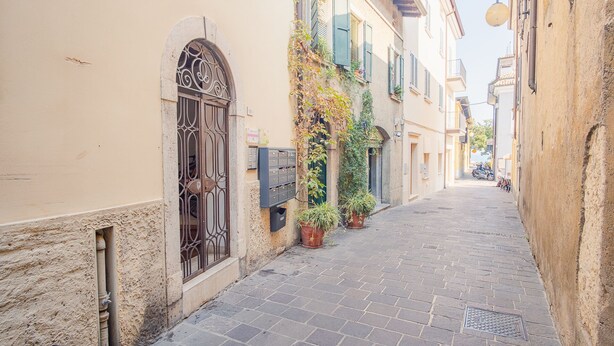 Une ruelle étroite pavée, bordée de bâtiments aux fenêtres en arc et agrémentée de plantes en pot.