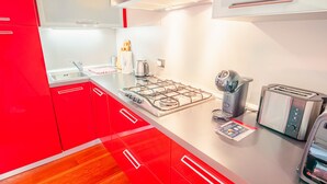 Une cuisine moderne avec des meubles de rangement rouges, une cuisinière à gaz, une machine à café et un grille-pain.