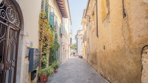 Une ruelle étroite pavée de pierres, bordée de bâtiments des deux côtés, dont certains sont dotés de volets et d’une boîte aux lettres.