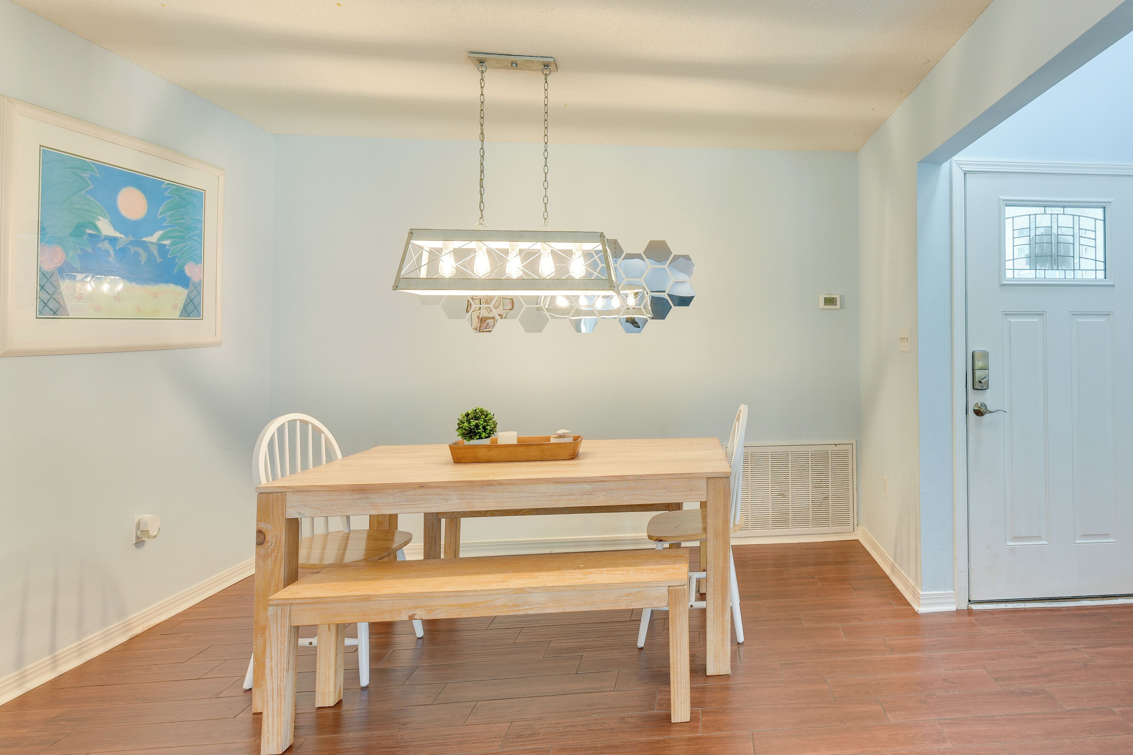 A dining area with a wooden table and benches, a hanging light fixture, and a door in the background.