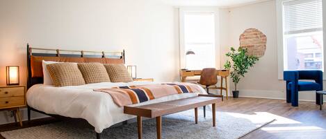 A modern bedroom with a wooden bed, a bench, a desk, and a chair.