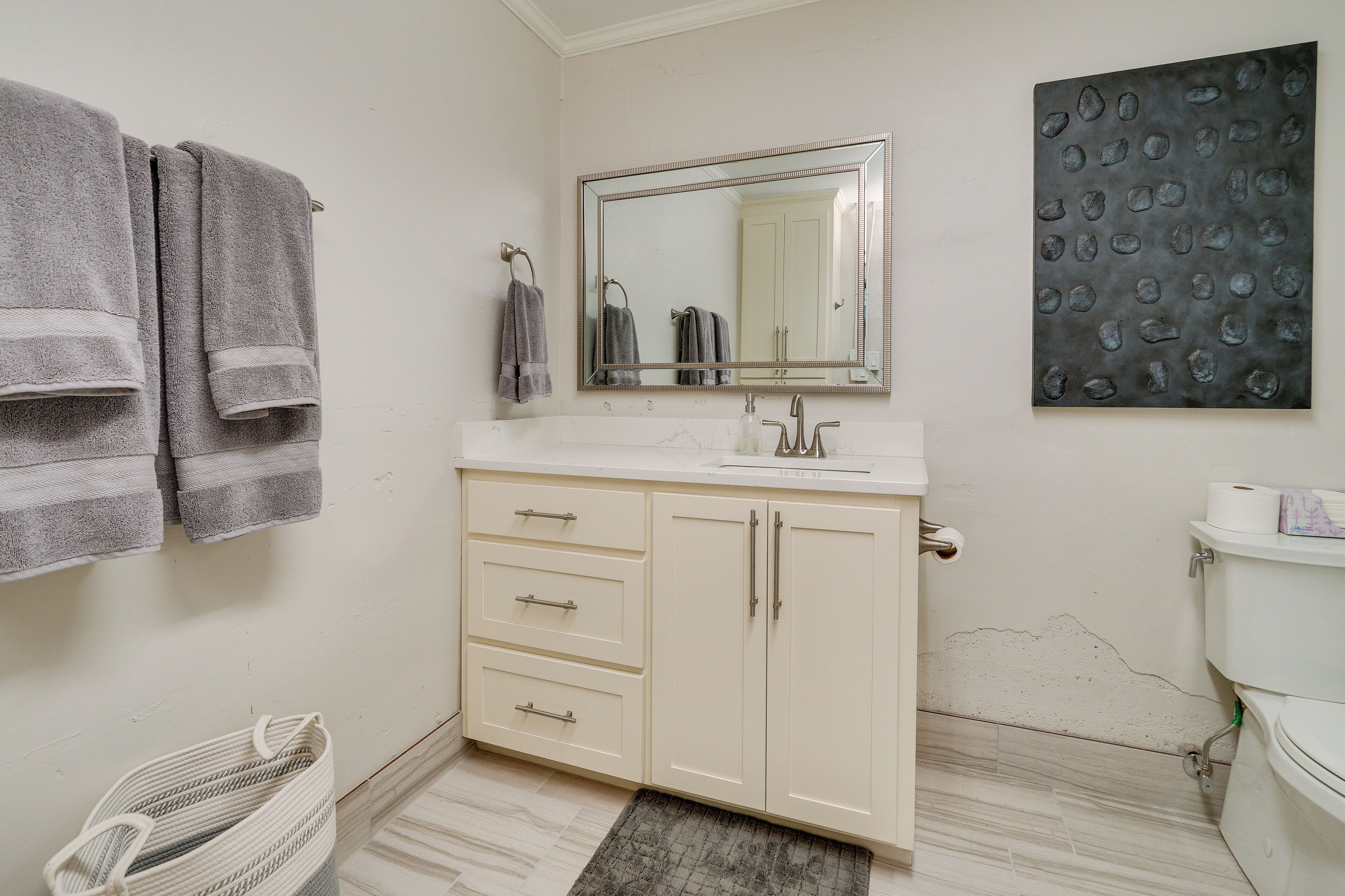 Une salle de bain avec un meuble-lavabo blanc, un grand miroir et deux serviettes suspendues à des crochets.