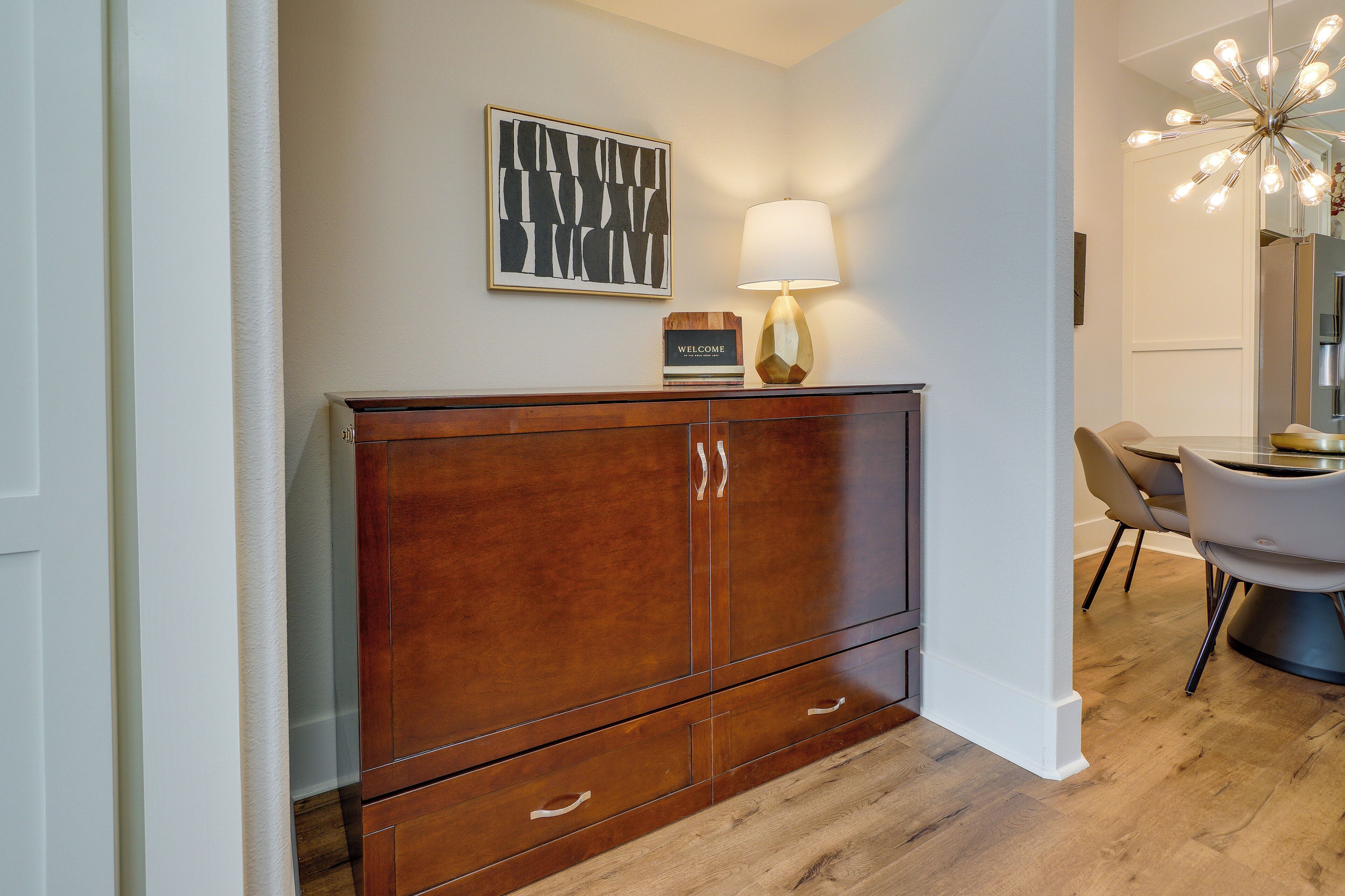A wooden cabinet with a welcome sign, a modern lamp, and a dining area with chairs and a table.