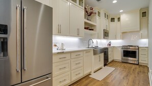 A modern kitchen with stainless steel appliances, white cabinetry, and wooden flooring.