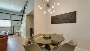 A dining area with a round table, six chairs, a chandelier, and a large abstract painting on the wall.