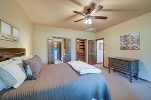 A bedroom with a large bed, a ceiling fan, a dresser, and a painting on the wall.