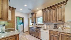A kitchen with wooden cabinets, granite countertops, a dishwasher, and a coffee maker. - Cozy Checotah Retreat w/ Deck Near Eufaula Lake (Checotah)