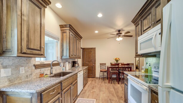 A kitchen with wooden cabinets, a granite countertop, a built-in oven, and a ceiling fan. - Cozy Checotah Retreat w/ Deck Near Eufaula Lake (Checotah)