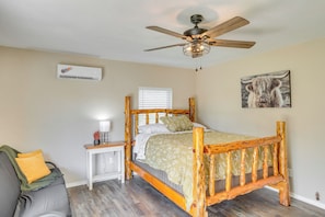 A bedroom with a wooden bed, a ceiling fan, a bedside table with a lamp, and a window with blinds. - Oklahoma Home Near Lake w/ Patio, Grill & Chiminea (Fort Cobb)