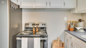 A kitchen with white cabinets, a stainless steel refrigerator, a stove with a towel, and a wooden cutting board. - Oklahoma Home Near Lake w/ Patio, Grill & Chiminea (Fort Cobb)