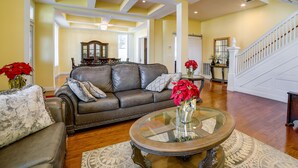 A spacious living room with a brown leather sofa, a glass coffee table, and a staircase leading to an upper level.