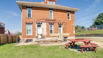 A two-story brick house with a front porch, a wooden fence, and a picnic table in the yard.