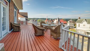 A wooden deck with wicker furniture and a table, overlooking a town with red-roofed buildings.
