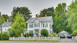 A two-story white house with green shutters, a white picket fence, and a garage with two cars parked inside. - 5 Mi to Salem: Furnished Patio at Danvers Studio! (Danvers)