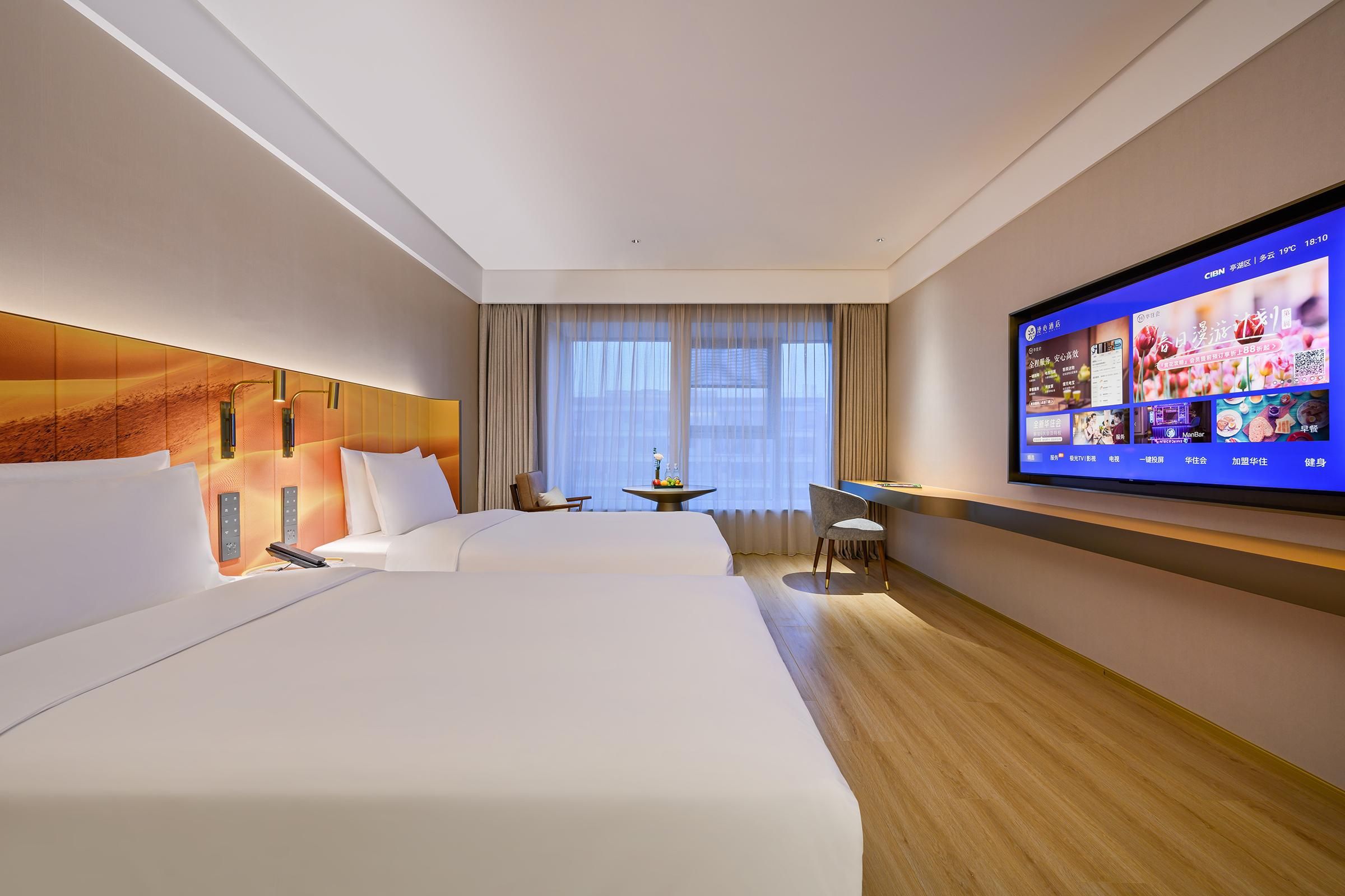 A hotel room with two beds, a desk, a chair, a TV, and a window with curtains.