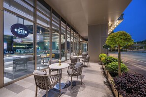A modern outdoor seating area with wicker chairs and round tables, a Costa Coffee sign, and a Manx Hotel in the background. - Manxin Hotel Yancheng Economic Development Zone (Yancheng)